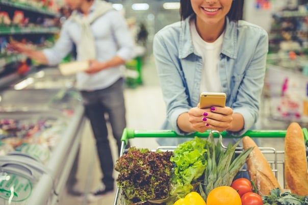 Women checks her shopping list on mobile while her partner browses the supermarket's product range