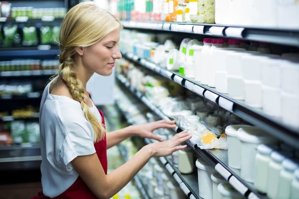 Woman shop assistant checking packaged dairy products on the supermarket shelves