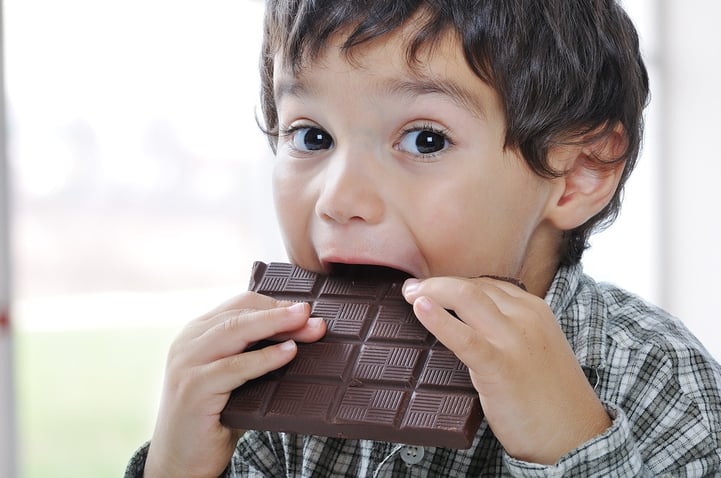 A little boy is about to take a bite out of an unwrapped block of milk chocolate.
