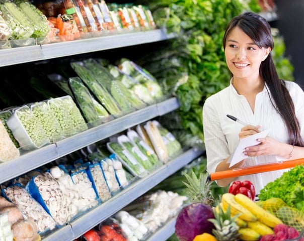 A woman with food in her shopping trolley who is texting at the supermarket.