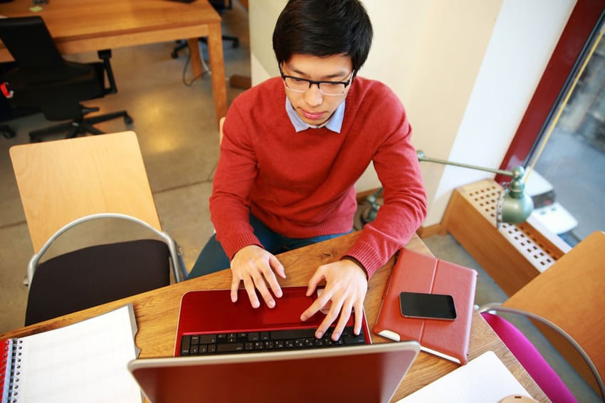 Young-asian-man-in-glasses-working-on-laptop-in-office